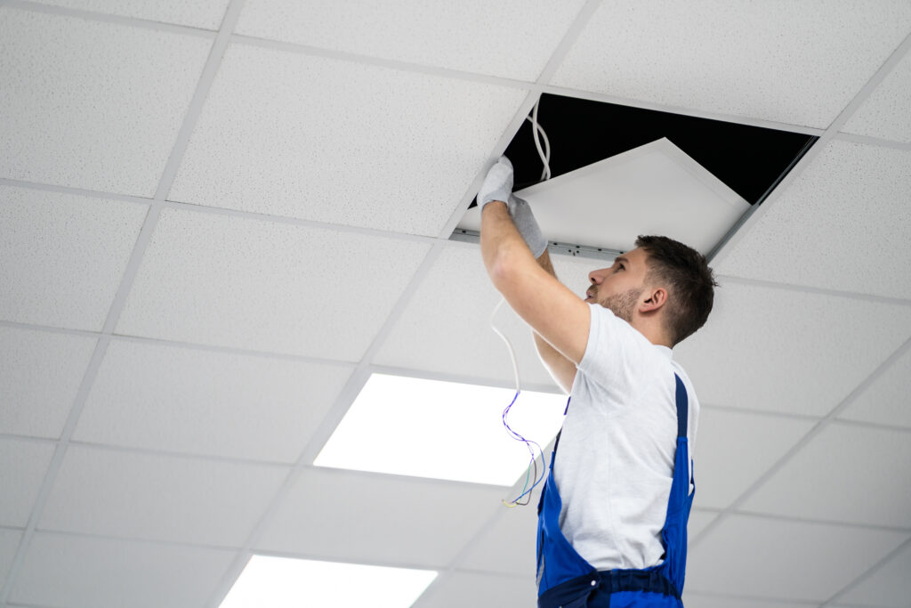 Electrician On Stepladder Installs Lighting To The Ceiling